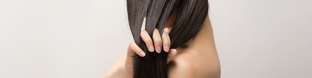 Mulher segura e separa mechas de cabelo longo, ilustrando queda capilar difusa associada ao eflúvio telógeno.