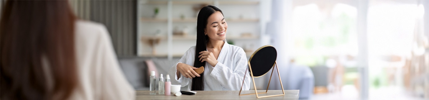 Mulher penteando os cabelos para espalhar bem o produto hidratante que ajuda a prevenir o surgimento de pontas duplas.
