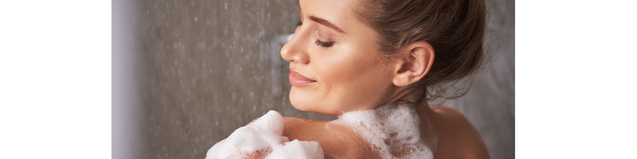 Mulher tomando um banho relaxante no chuveiro usando um sabonete de argila para limpar e nutrir a pele