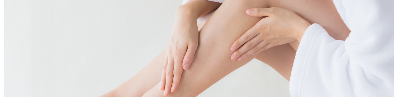 Mulher aplicando hidratante na perna como rotina de hidratação da pele.