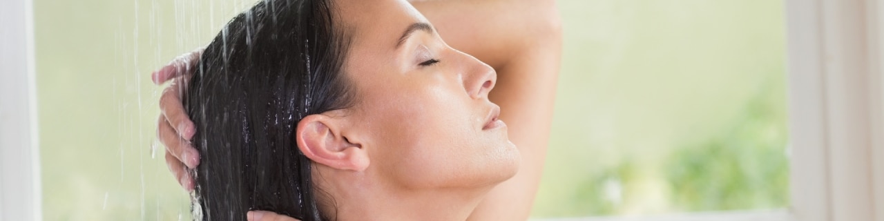 Mulher de olhos fechados lavando os cabelos, aplicando produtos de detox capilar para purificar o couro cabeludo.