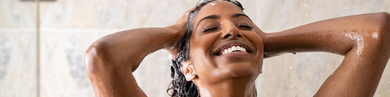 Mulher no chuveiro com expressão de felicidade usando um shampoo para cabelos cacheados