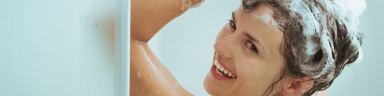 Mulher no chuveiro  lavando o cabelo com shampoo antirresíduo